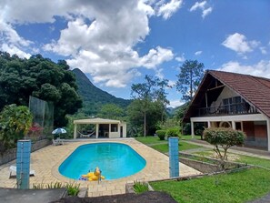 Une piscine avec un hamac et un chien gonflable jaune, entourée de verdure et avec une montagne en arrière-plan.