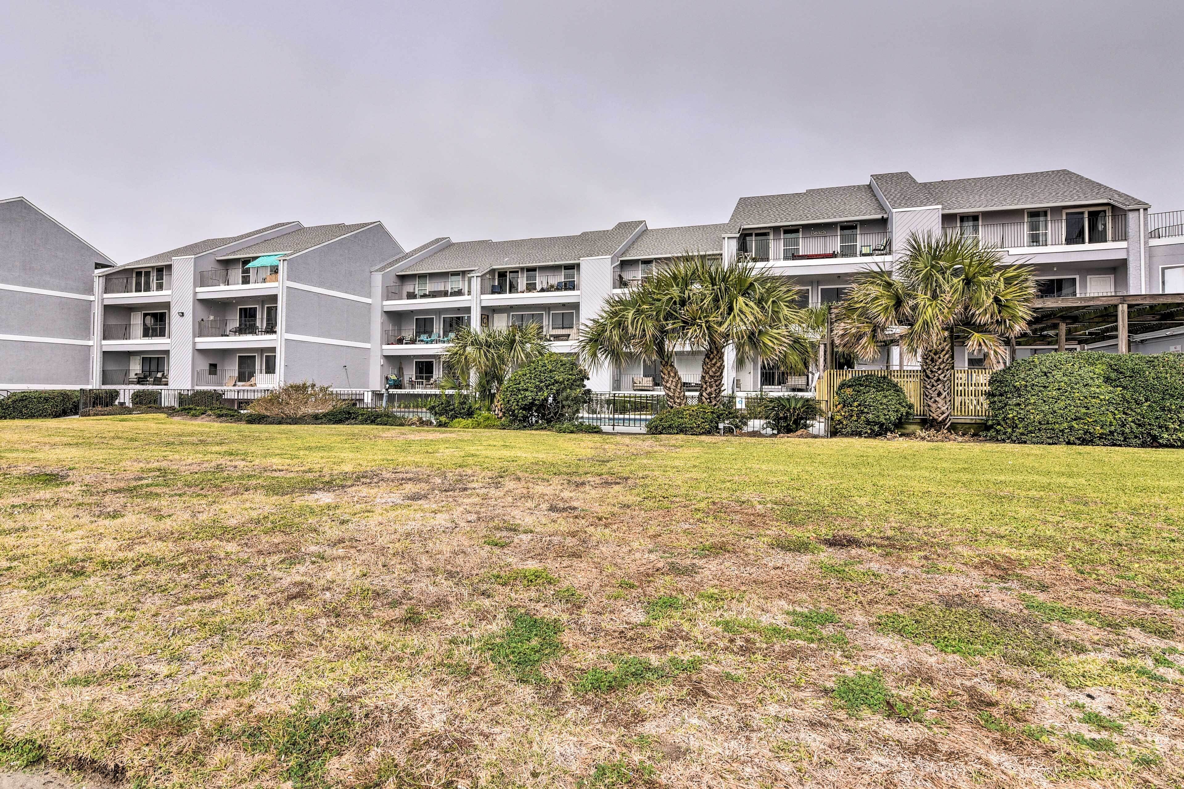 A multi-story residential building with balconies, a grassy lawn, and palm trees.