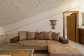 A modern living room with a sectional sofa, a wooden ceiling, and a wooden door.