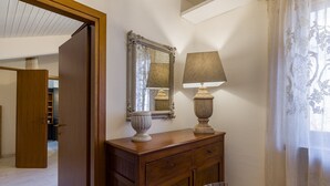 A wooden dresser with a mirror and a lamp, a chair, and a wooden table in a room with a wooden floor and a door leading to another room.