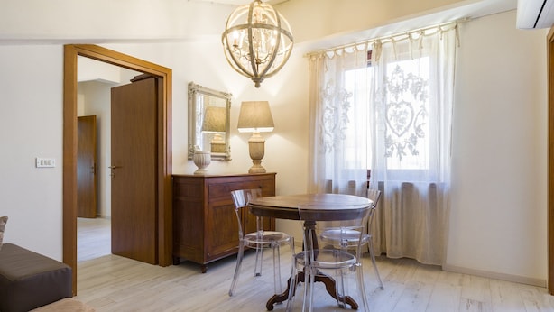 A dining area with a round table, clear chairs, a wooden cabinet, a lamp, and a chandelier.