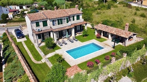 Ein zweistöckiges Haus mit Swimmingpool, einer Terrasse mit Liegestühlen und einem Garten.