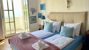 Ein Schlafzimmer mit einem großen Bett, einem Nachttisch, einer Lampe und Blick ins Freie durch eine Schiebetür.