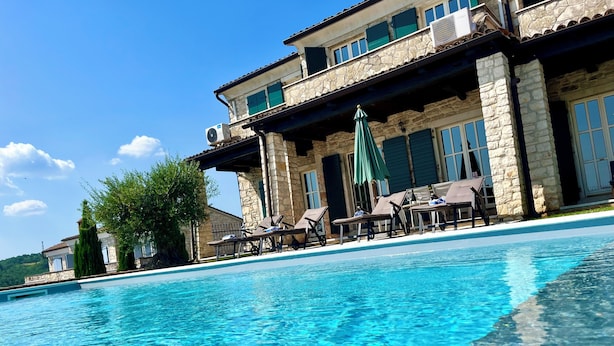 Ein klares Schwimmbecken mit Liegestühlen und Sonnenschirmen, umgeben von Steingebäuden mit zahlreichen Fenstern und Balkonen.