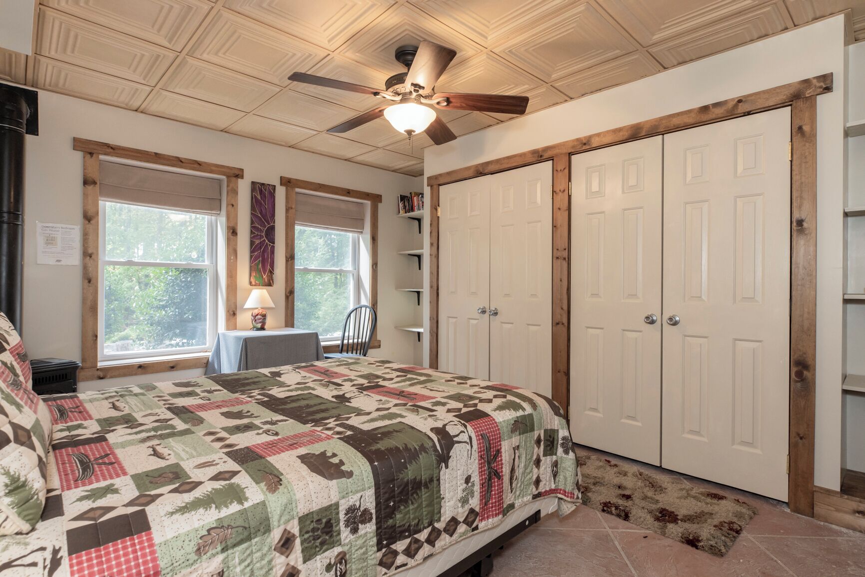 Een slaapkamer met een bed, een plafondventilator, een raam, een bureau en een kledingkast.