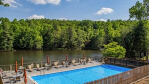 An outdoor swimming pool with lounge chairs and umbrellas, surrounded by a wooden fence and a forested area.