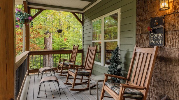 A wooden porch with rocking chairs, a small Christmas tree, and a sign inviting visitors to sit on the porch.