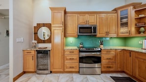 Uma cozinha com armários de madeira, eletrodomésticos de aço inoxidável, um revestimento verde e um espelho redondo.