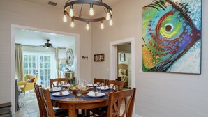Un coin repas avec une table ronde en bois, dressée pour quatre personnes, un lustre et une peinture abstraite aux couleurs vives accrochée au mur.