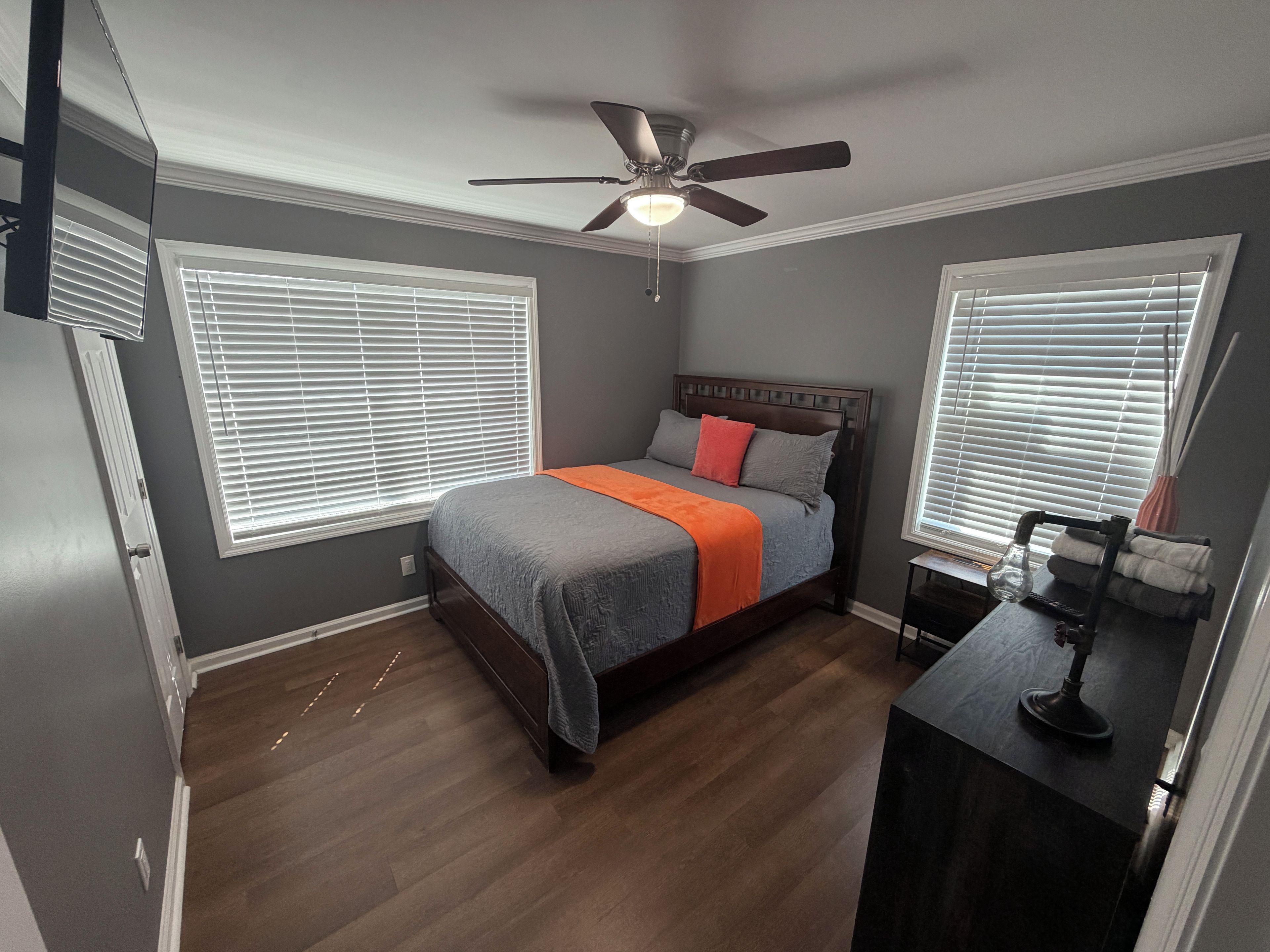 Un dormitorio con una cama, un ventilador de techo y dos ventanas con persianas.