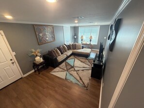 Een woonkamer met een hoekbank, een flatscreen televisie en een decoratief vloerkleed.
