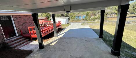 A covered patio area with a concrete floor, a red play structure, and a brick building in the background.