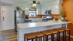 A kitchen with a central island, bar stools, a refrigerator, a stove, and a ceiling fan. - Walk to Beach: PCB Condo w/ Oceanfront Pool Access (Panama City Beach)