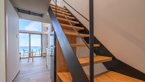 Una escalera moderna con escalones de madera y barandillas de metal, que conduce a una habitación con vistas al mar.