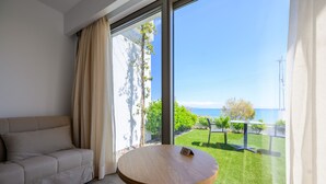 Una habitación moderna con sofá, una mesa redonda de madera y un ventanal con vistas a un césped verde y al mar.