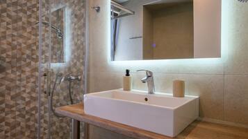A bathroom with a shower, a sink with a mirror, and a wooden countertop.
