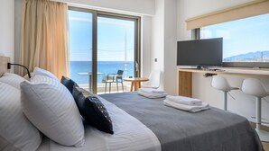 Habitación de hotel con cama, escritorio con televisor, silla, mesita y vista al mar.