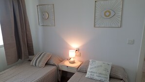 A room with two single beds, a nightstand with a lamp, and two wall-mounted decorative items. - Infante E2-9 Solo Familias! (Playa de Gandía)