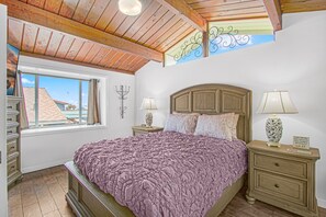 Un dormitorio con una cama grande, cabecera de madera, dos mesitas de noche con lámparas, una ventana con cortinas y vistas al exterior.