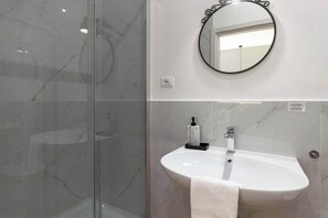 A bathroom with a glass shower enclosure, a white sink with a towel, and a round mirror on the wall. - Amazing Studio in the City Center ★ Fast Wifi (Trieste)