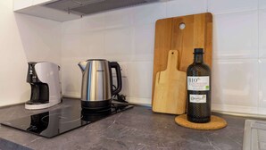 Una cocina con cafetera, hervidor, tabla de cortar y una botella de vino.