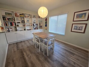 Una cocina con armarios blancos, una mesa de comedor de madera y una lámpara colgante.