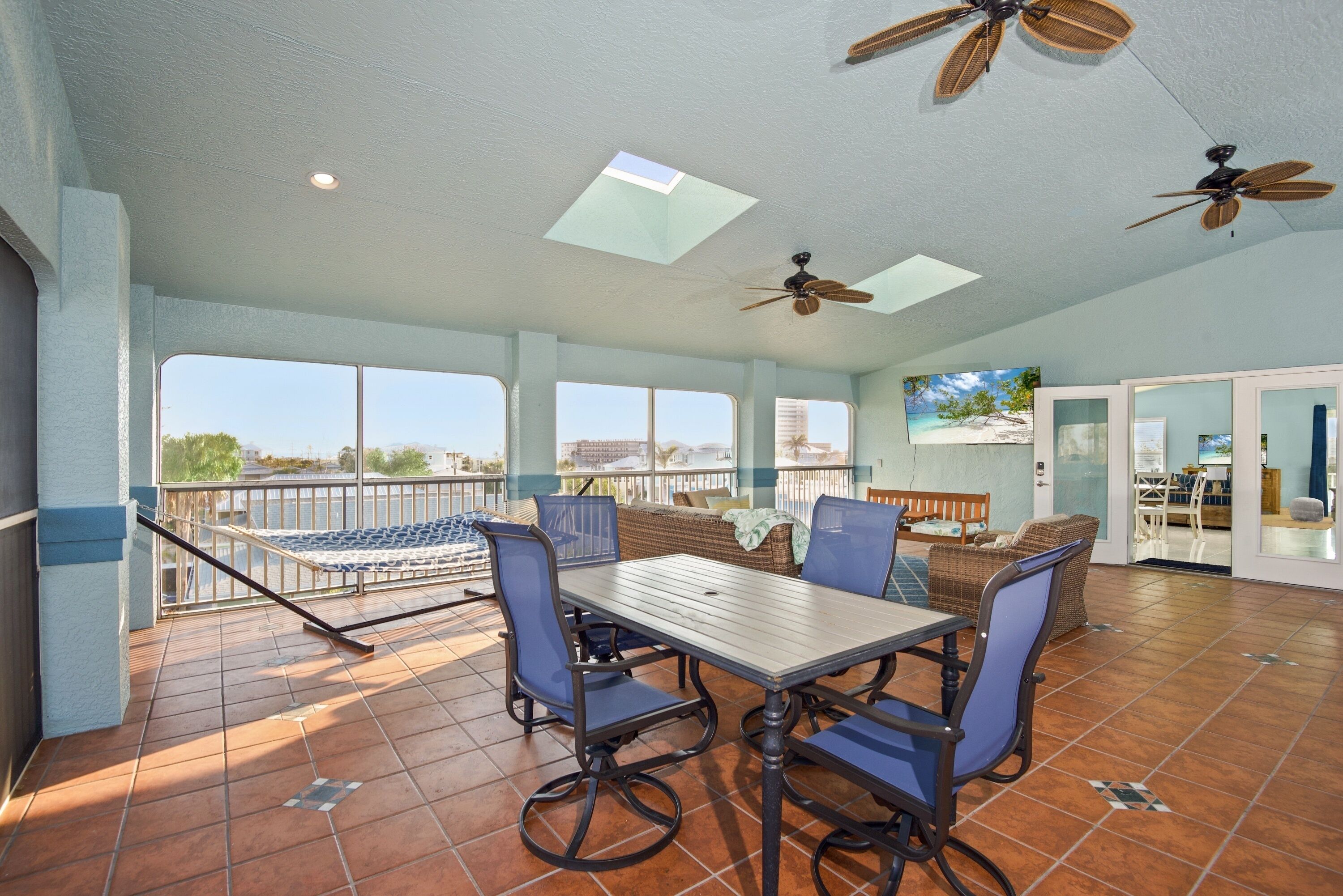 A spacious patio with a dining table, chairs, and a sofa. There are ceiling fans and a view of the city through large windows.