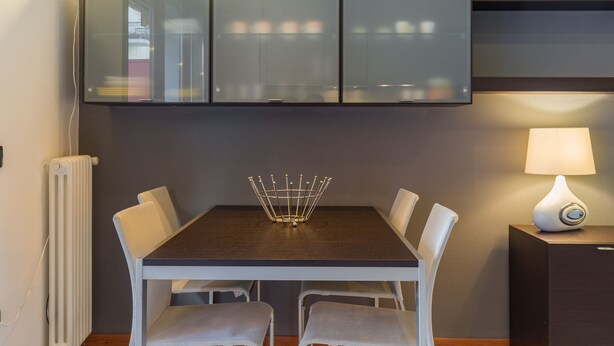 A dining area with a table, chairs, a cabinet, a lamp, and a radiator. - Le Volpi in città (Verona)