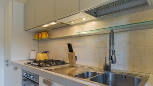 A modern kitchen with a stainless steel sink, a gas stove, and white cabinetry. - Le Volpi in città (Verona)