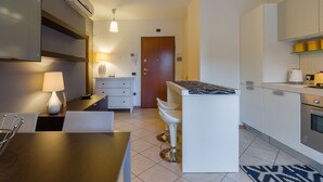 A modern kitchen with a central island, white bar stools, a dining table, and a TV mounted on the wall. - Le Volpi in città (Verona)