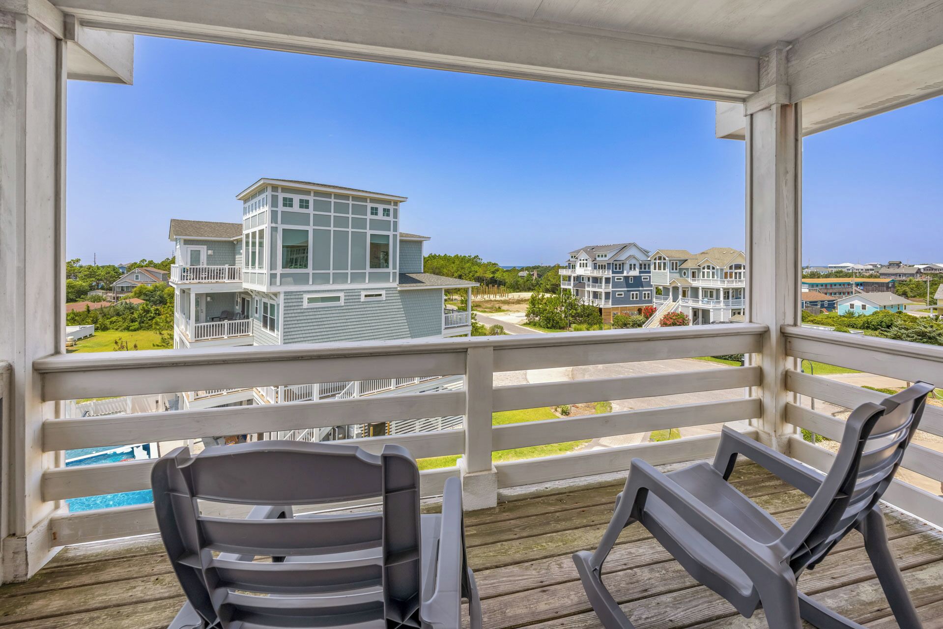 A balcony with two chairs, overlooking a coastal residential area with modern houses.