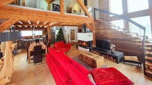Un amplio salón con techo alto, vigas de madera, un sofá rojo, una chimenea, un televisor y una escalera.
