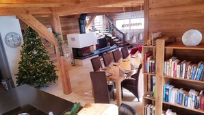 Un interior acogedor de madera con comedor, una estantería, un árbol de Navidad y una cocina con estufa.