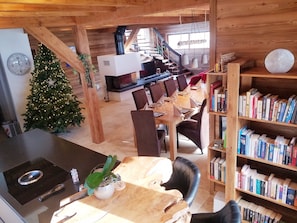 Um interior de madeira acolhedor com área de jantar, estante de livros, árvore de Natal e cozinha com fogão.