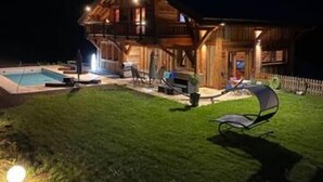 Una cabaña de madera con piscina, mobiliario exterior y una zona de patio bien iluminada.