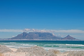 A coastal landscape with a mountain range and a city in the background.