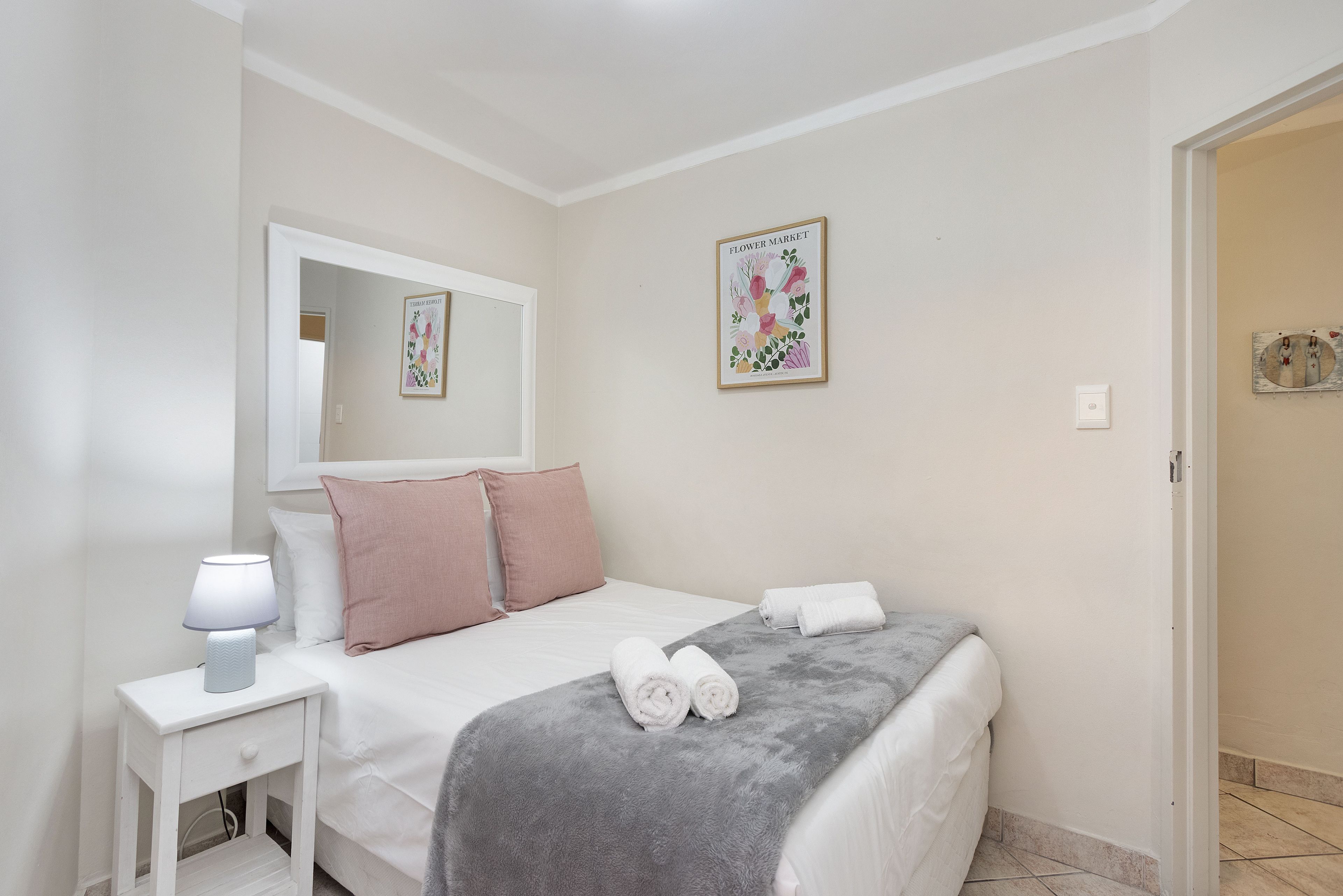 Un dormitorio con una cama, almohadas, una mesita de noche con lámpara, una colcha y una obra de arte en la pared.