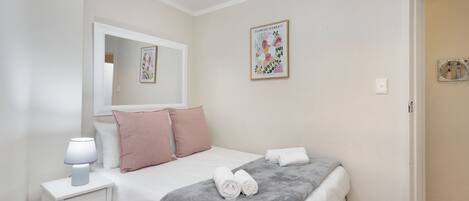 Un dormitorio con una cama, almohadas, una mesita de noche con lámpara, una colcha y una obra de arte en la pared.