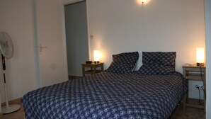 A bedroom with a bed, two bedside lamps, a standing fan, and a door. - Villa close to the beach with exceptional views. (Port-la-Nouvelle)