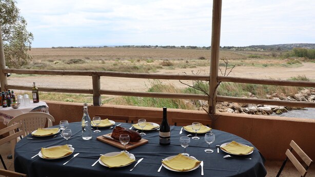 A table set for a meal with a bottle of wine, glasses, and plates, overlooking a natural landscape. - Villa close to the beach with exceptional views. (Port-la-Nouvelle)