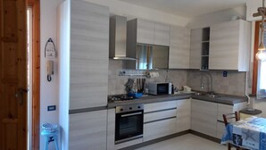A modern kitchen with stainless steel appliances, a built-in oven, and a dining area with a table set for two. - Newly furnished two-room apartment, 800 mt from the sea. (Cecina)