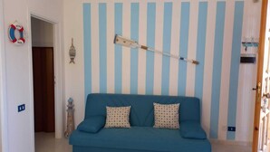 A room with a blue-striped wall, a blue sofa with patterned cushions, a life ring, a fish decoration, and a lighthouse ornament. - Newly furnished two-room apartment, 800 mt from the sea. (Cecina)