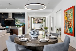A modern dining area with a round table, grey upholstered chairs, and a central floral arrangement. - Stay in 3rd Rock Home ! (Palm Springs)