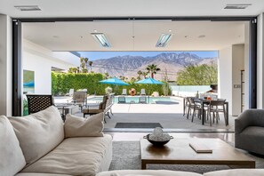 A modern living room with a large glass door leading to a pool area, outdoor furniture, and a mountain view. - Stay in 3rd Rock Home ! (Palm Springs)