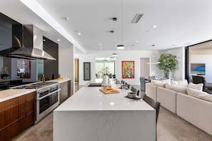 A modern kitchen with a central island, stainless steel appliances, and a seating area with a sofa and chairs. - Stay in 3rd Rock Home ! (Palm Springs)