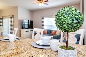 Une cuisine moderne avec un plan de travail en granit, un arbre bonsai en pot et un coin repas avec des chaises blanches et une table dressée avec des assiettes et des tasses.