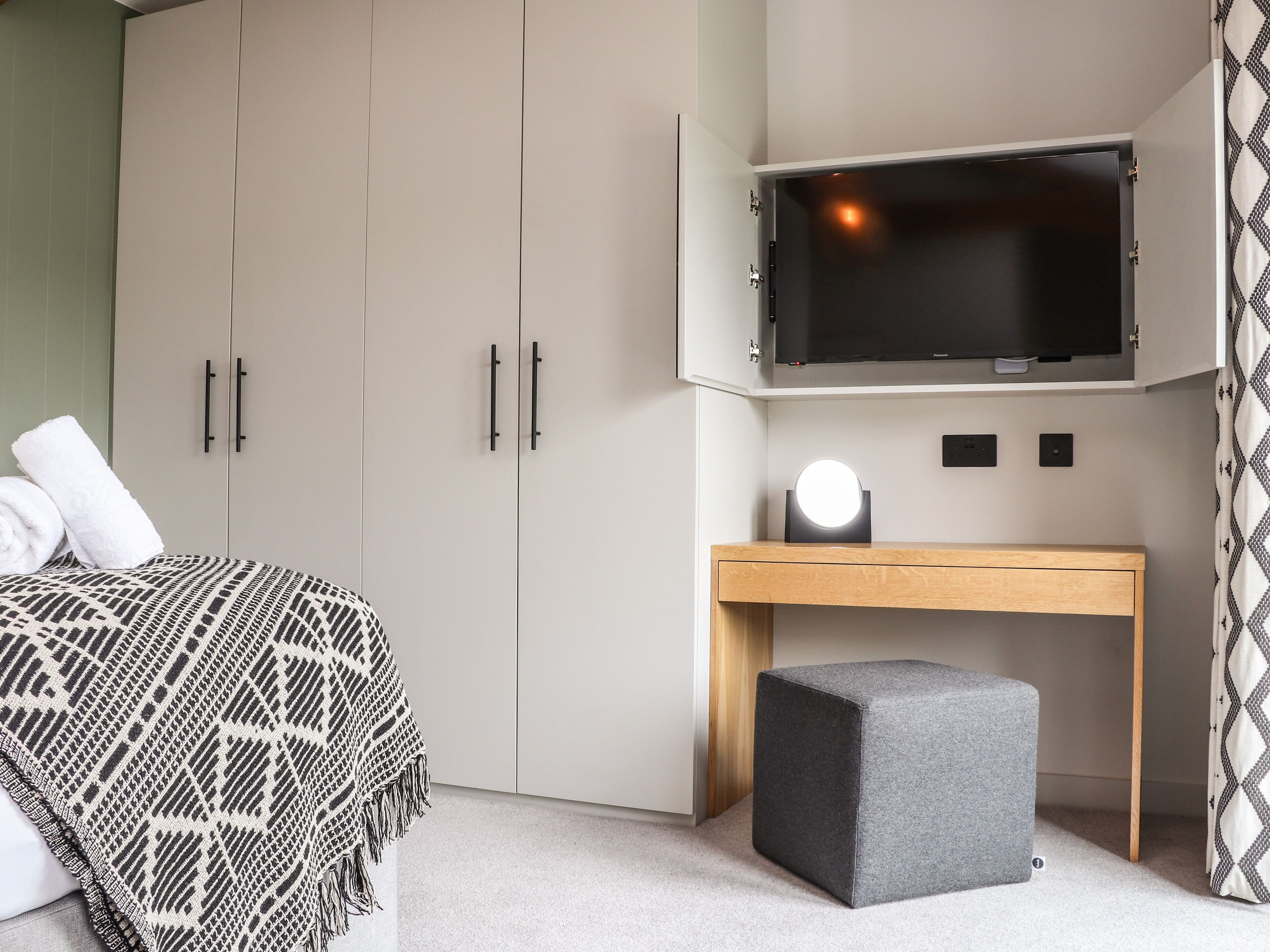 Un dormitorio con cama, un escritorio con televisor y un pequeño reposapiés.