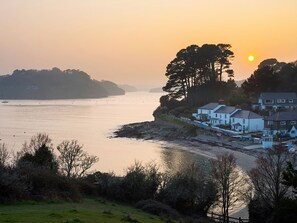 A coastal village with houses along the shoreline, a calm sea, and a setting sun.