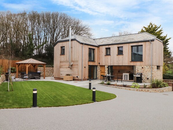 A modern two-story house with a covered outdoor area, stone walls, and a well-maintained lawn.