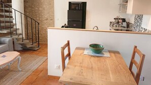Et kompakt køkken med en central ø, et spisebord med stole, en stenvæg og en trappe til et andet niveau.